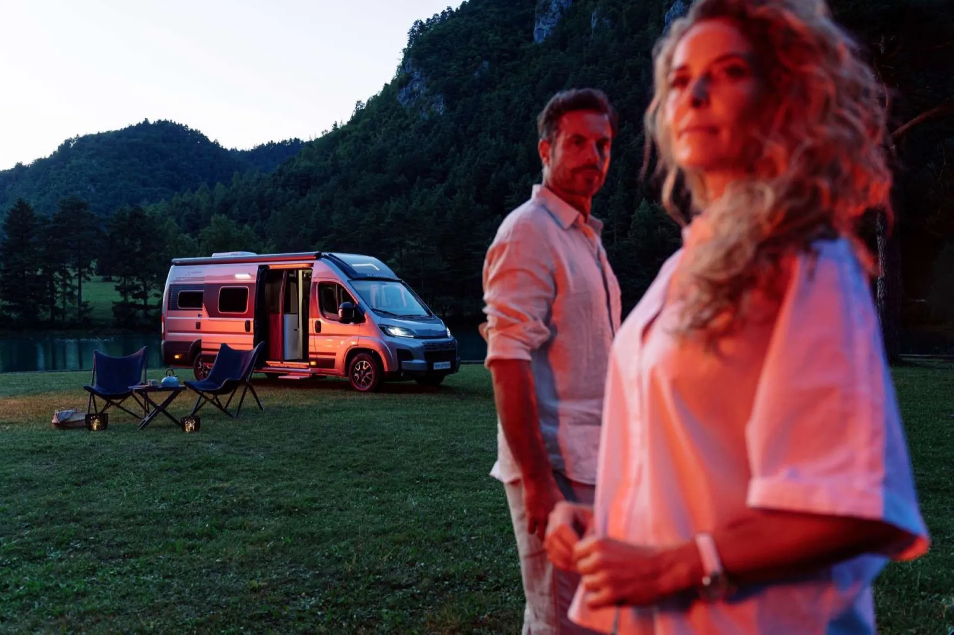 Couple au crépuscule devant leur camping-car Neo-NOMAD aménagé, au bord d'un lac de la région Sud Provence-Alpes-Côte-d’Azur